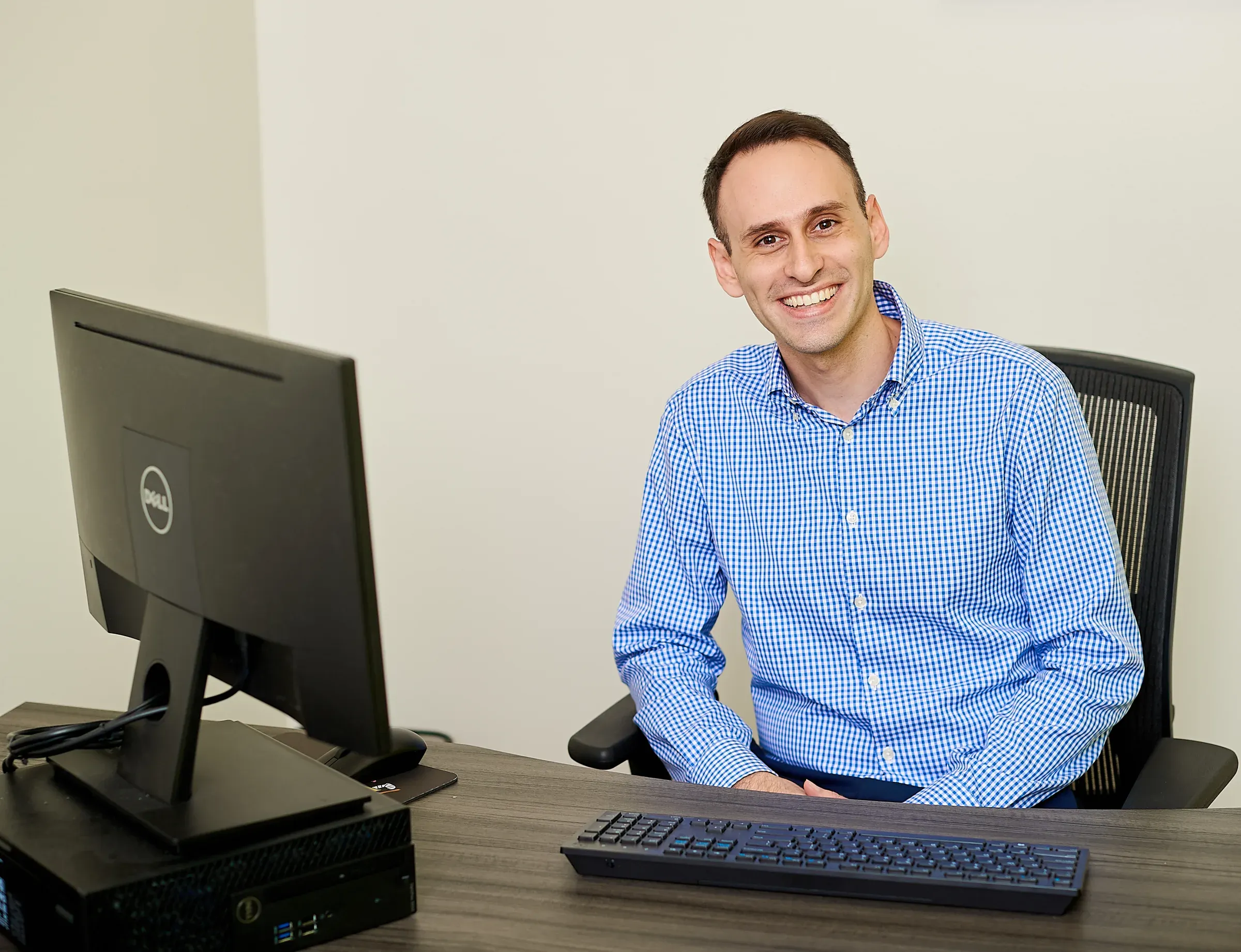 Salvador H. Bou at his workstation, smiling, in a blue checked shirt
